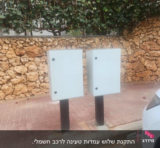 שני ארונות חשמל על מדרכה ליד קיר אבן